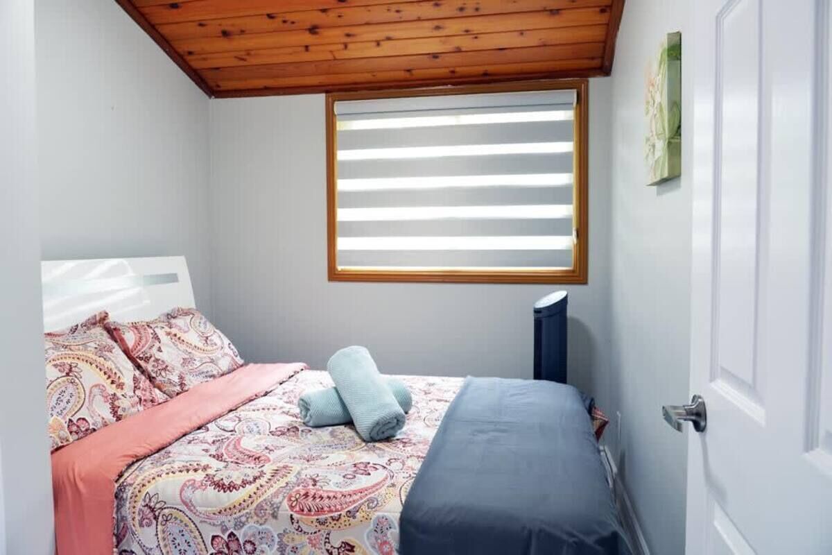 A bedroom with a bed, a window with blinds, a door, and a wall-mounted artwork.