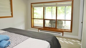 Ein Schlafzimmer mit großem Fenster, einem Bett mit gemustertem Überwurf und einer Sitzbank darunter.