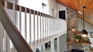 Ein mehrstöckiger Innenraum mit einer Holztreppe, einem Steinofen und einer hängenden Leuchte.