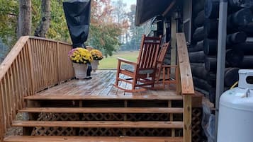 Une terrasse en bois avec une chaise et un jardinière, qui mène à un chalet en rondins.