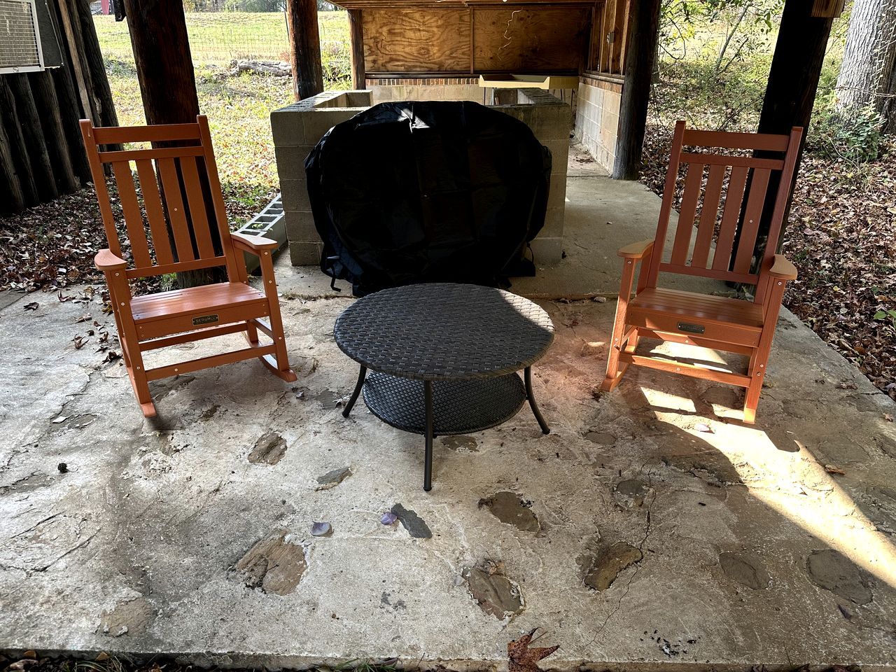 Zwei Holzstühle und ein runder Tisch auf einer Betonpatio mit einem Grill im Hintergrund.