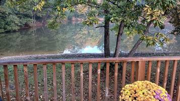 A wooden deck with a railing overlooking a calm body of water, surrounded by trees and foliage.