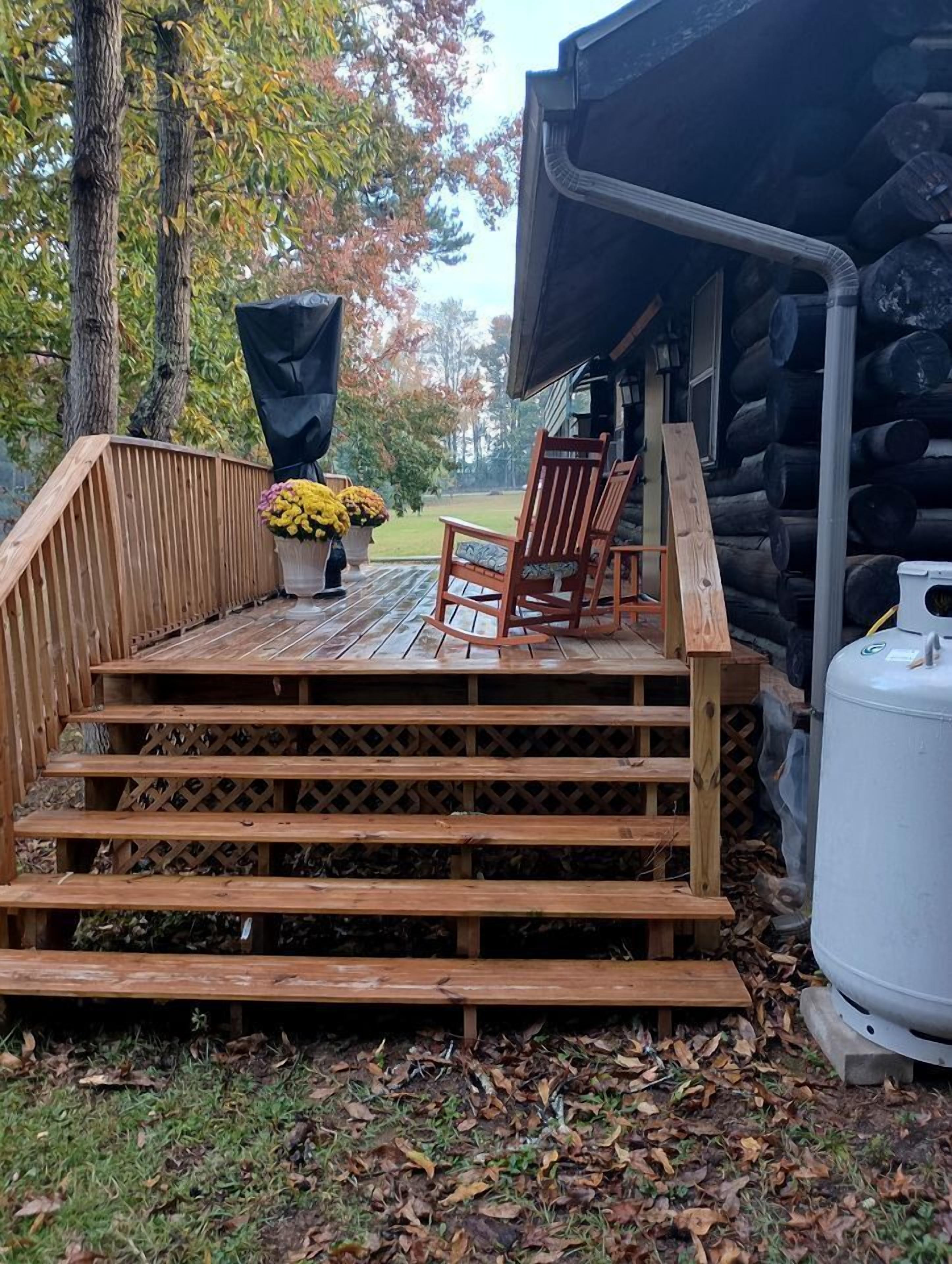 Eine Holzterrasse mit Stuhl und Pflanzgefäß, die zu einer Blockhütte führt.