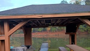 A wooden pavilion with a concrete floor, a picnic table, and a covered grill area.