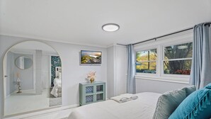 Un dormitorio con un espejo grande, una cama con almohadas, un armario pequeño y una ventana con cortinas.