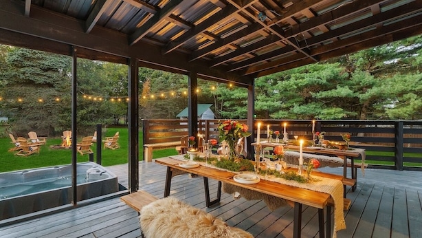 Terraza exterior con mesas de madera dispuestas para comer, rodeada de sillas y un jacuzzi.