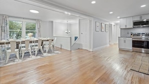 Una cocina amplia con armarios blancos, un horno de acero inoxidable y un comedor con mesa y sillas de madera.