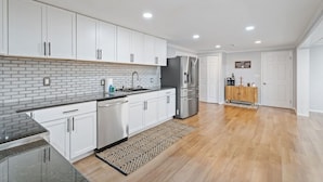 Una cocina moderna con armarios blancos, salpicadero de ladrillo, electrodomésticos de acero inoxidable y suelo de madera.