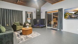 Una sala de estar moderna con sofá, sillón y una mesa redonda de centro. Hay un ventanal con cortinas, una chimenea y una vista panorámica de montañas.