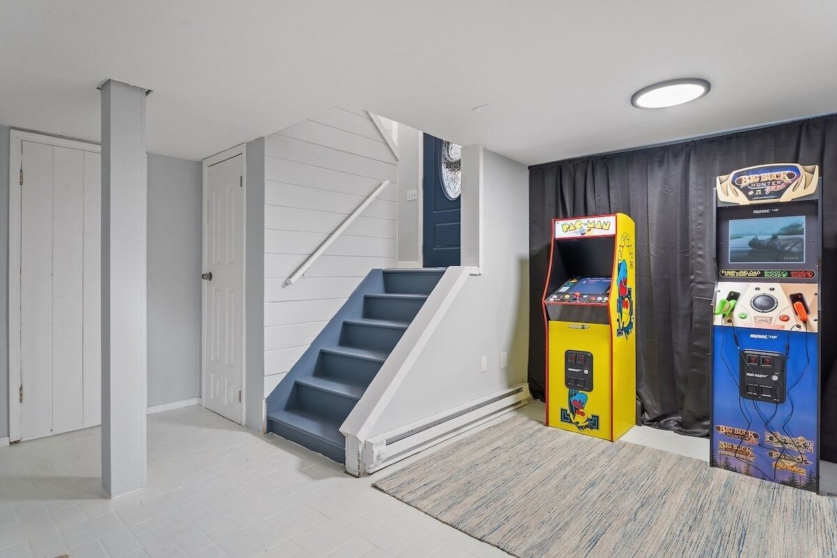 Une pièce avec un escalier, deux bornes d’arcade et une porte.