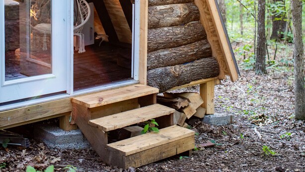 A log cabin with a glass door entrance, wooden steps, and a hanging chair inside. - Lake Of The Ozarks Tiny Aframe in the woods (Lincoln)