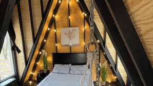 A cozy attic bedroom with a bed, hanging chair, and string lights. - Lake Of The Ozarks Tiny Aframe in the woods (Lincoln)