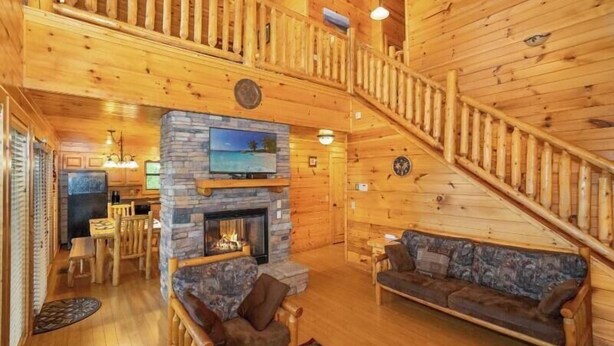 A log cabin interior with a stone fireplace, wooden furniture, a dining area, and a staircase. - Bearly Chocolate (Sevierville)