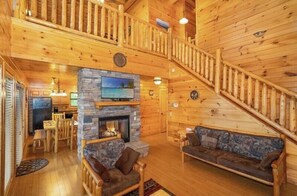 A log cabin interior with a stone fireplace, wooden furniture, a dining area, and a staircase. - Bearly Chocolate (Sevierville)