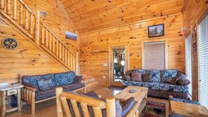 A wooden cabin interior with a staircase, two sofas, a coffee table, and a window with blinds. - Bearly Chocolate (Sevierville)