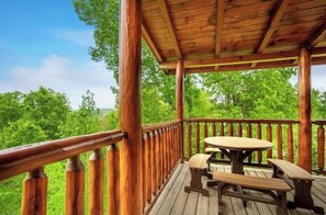 Eine Holzterrasse mit Picknicktisch und Bänken, umgeben von üppigem Grün.
