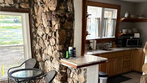 Une cuisine aux murs en pierre, un coin repas avec une table et des chaises, et une vue sur l’extérieur.