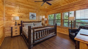 A wooden cabin bedroom with a bed, bedside tables, lamps, a ceiling fan, and large windows. - Majestic View (Sevierville)