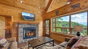 A cozy cabin interior with a stone fireplace, wooden walls, and a large window offering a mountain view. - Majestic View (Sevierville)