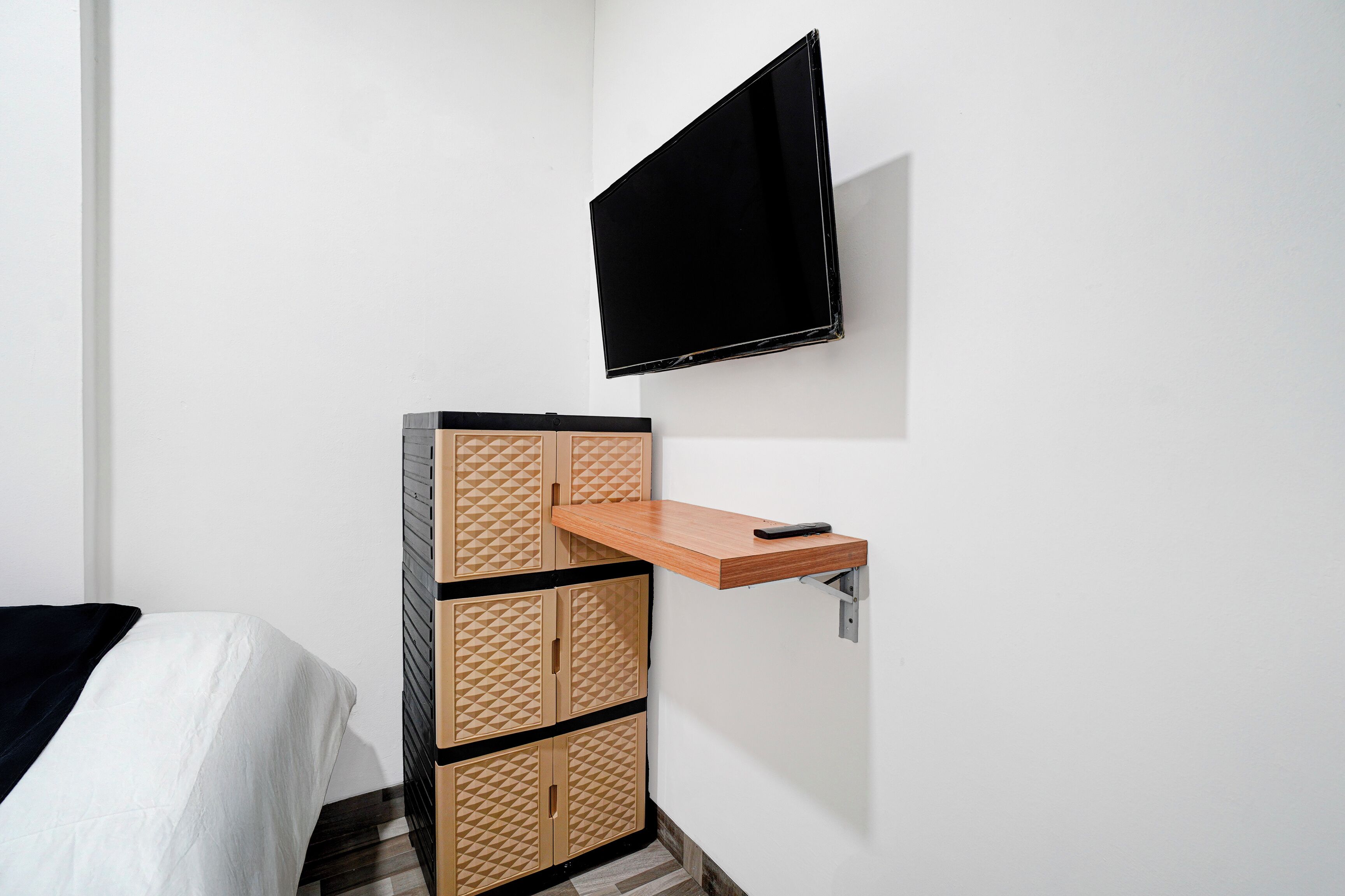 Un dormitorio con una cama, un televisor montado en la pared y un mueble de madera con cajones.