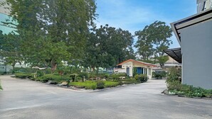 A spacious parking lot with a small building in the center, surrounded by lush greenery and trees. - Capital O 94914 Kemayoran Guest House (Jakarta)