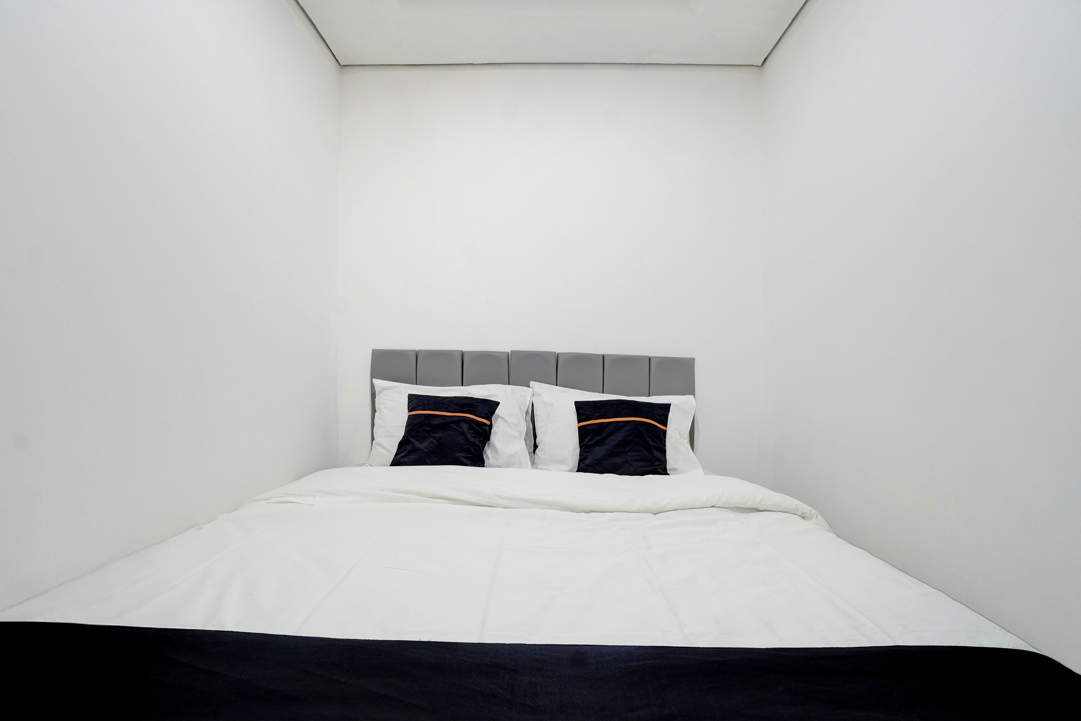 A bed with a white mattress and dark bedding, a grey headboard, and two pillows with orange stripes.