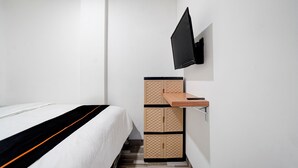 A hotel room with a bed, a TV mounted on the wall, and a wooden cabinet with drawers. - Capital O 94914 Kemayoran Guest House (Jakarta)
