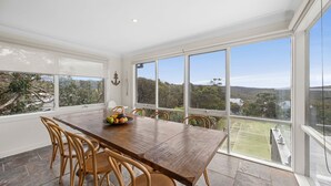 A dining area with a wooden table and chairs, large windows with a view of a landscape. - Rally House Fairhaven (Fairhaven)