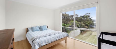 Ein Schlafzimmer mit einem Bett, einer Holzkommode und einem großen Fenster mit Gartenblick.