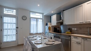 Una cocina moderna con armarios blancos, una mesa de comedor preparada para seis personas y un reloj en la pared.