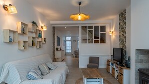 Una sala de estar moderna con sofá, mesa de centro y televisor. Se ven estanterías con objetos decorativos y una chimenea.