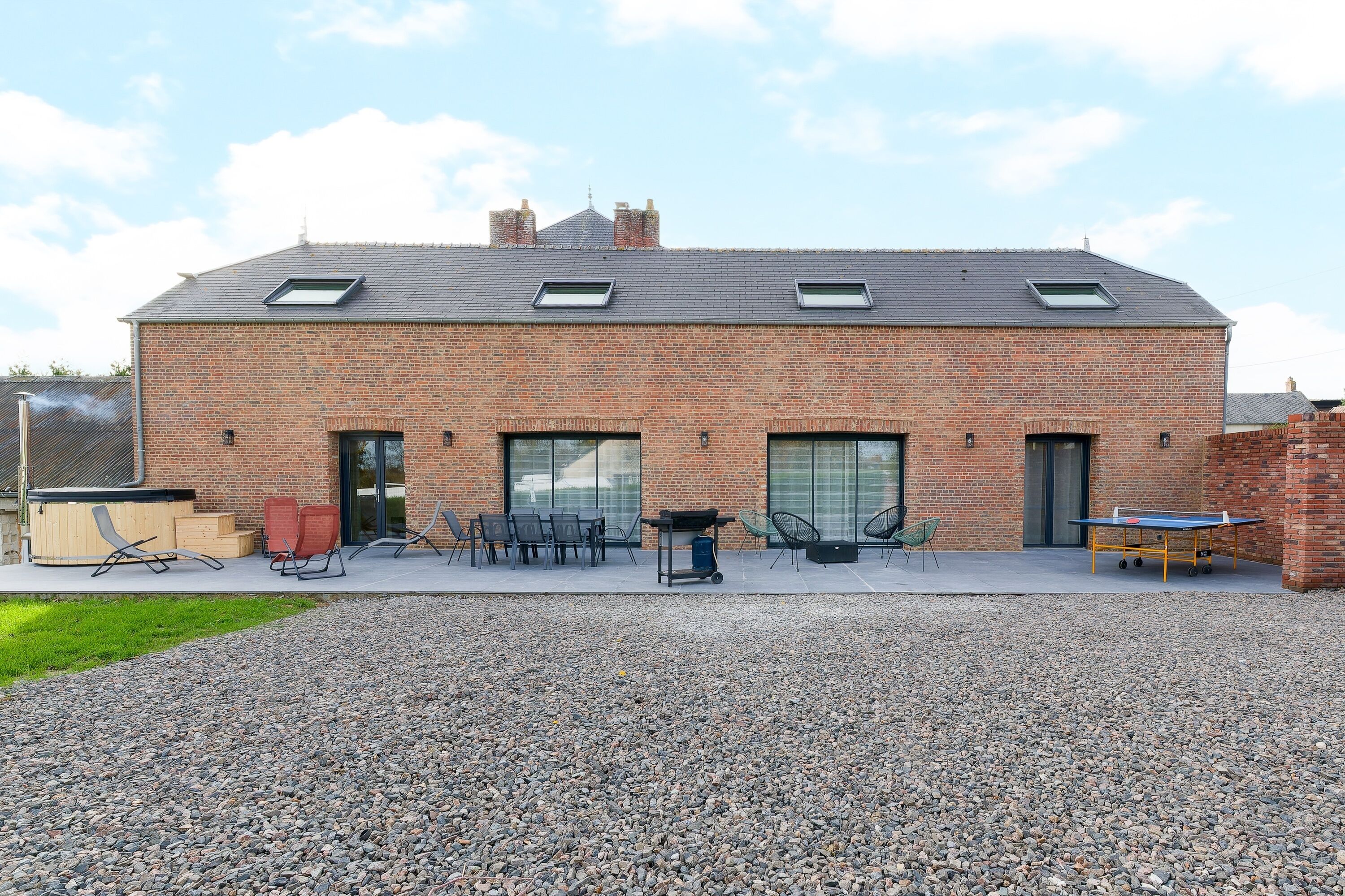 A brick building with a flat roof, large windows, and outdoor seating area with tables and chairs.