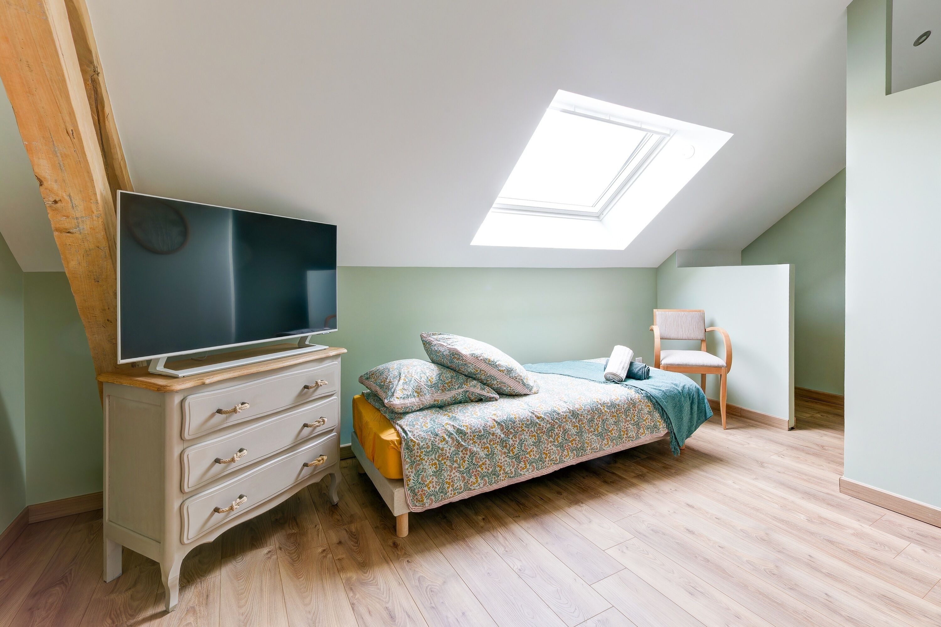Un dormitorio con cama, cómoda, televisor y tragaluz.