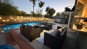 Uma área à beira da piscina com hidromassagem, assentos e uma parede de tijolos com iluminação.