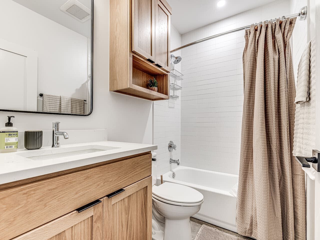 Ein modernes Badezimmer mit einem Holzkonsolenunterschrank, einem weißen Waschbecken, einem Spiegel, einer Dusche mit beiger Duschvorhang und einer weißen Toilette.