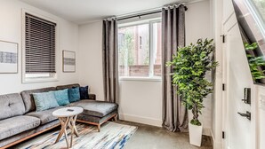 Ein modernes Wohnzimmer mit einem grauen Sofa, einem kleinen runden Couchtisch und einer großen Topfpflanze.