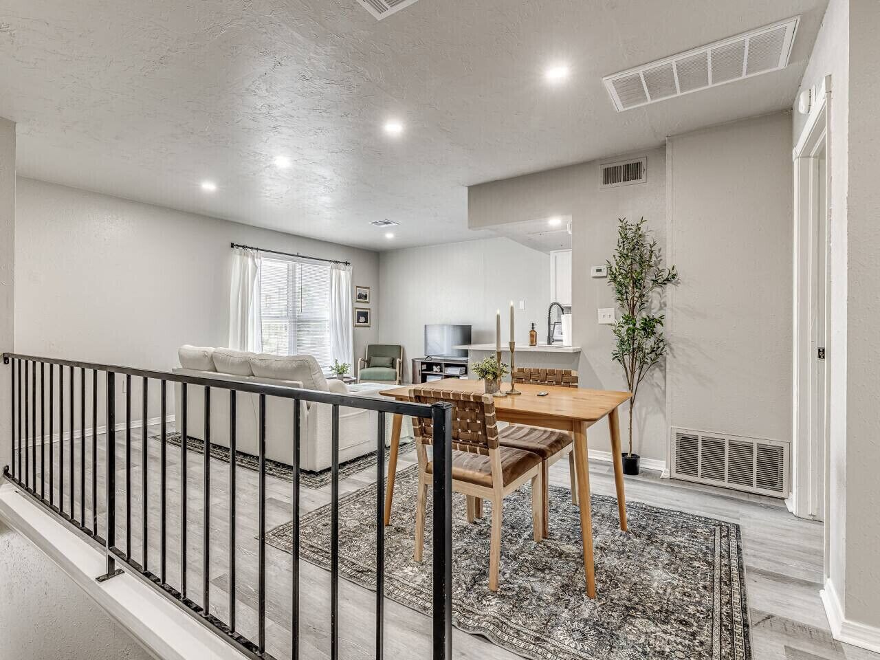 A spacious living area with a dining table, chairs, and a sofa. There is a TV, a plant, and a window with curtains.