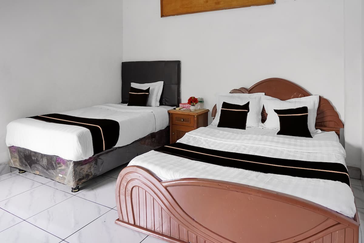 Two beds with black and white bedding, a wooden nightstand with a vase of flowers, and a plain white wall.