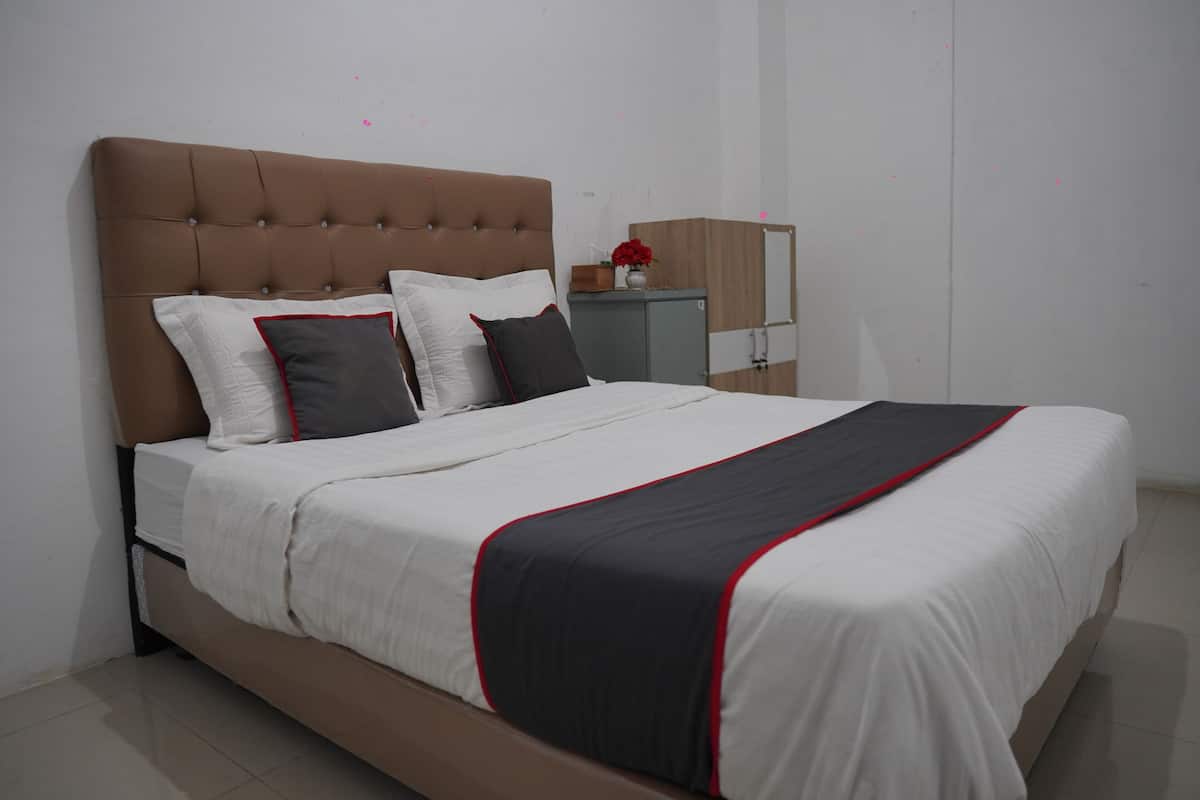 A modern bedroom with a tufted headboard, a large bed with white bedding and a black and red accent, a nightstand with a vase of flowers, and a mirror on the wall.