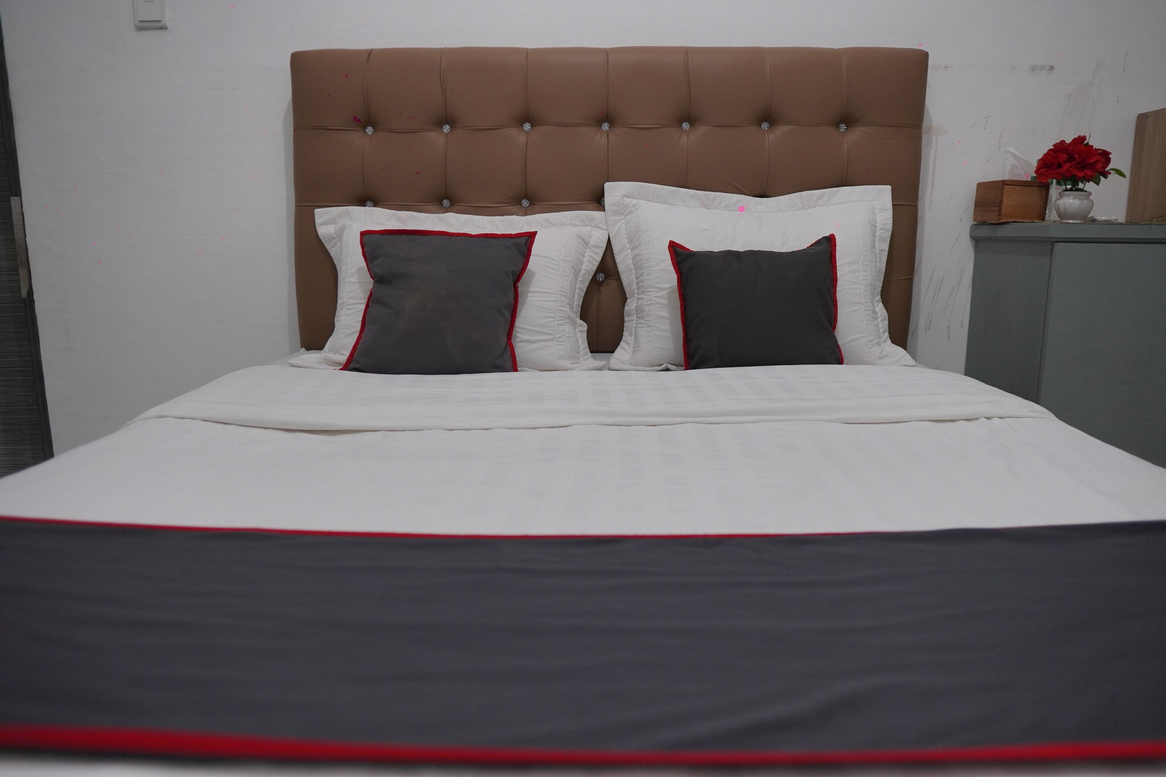 A bed with a tufted headboard, white bedding, and two pillows with red trim.