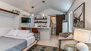 Ein kleines Hotelzimmer mit einem Bett, einem Schreibtisch, einem Sessel, einer Couch, einer Lampe und einem Fernseher.
