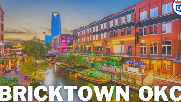 Vista del río Bricktown con edificios, un bote y un rascacielos azul destacado.