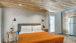 Un dormitorio con cama, mesitas de noche, un espacio de cocina con armarios y un refrigerador.