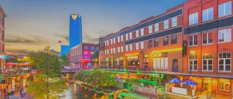 Vue sur Bricktown depuis la rive, avec ses bâtiments, un bateau et un imposant gratte-ciel bleu qui se distingue.