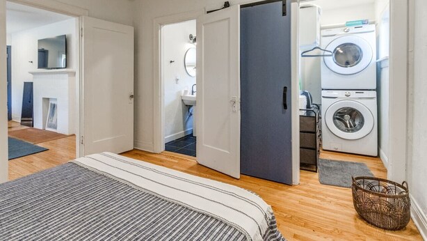 A bedroom with a bed, a gray striped rug, a dark door, and a laundry area with a washing machine and dryer. - Updated Garage Apartment (Oklahoma City)
