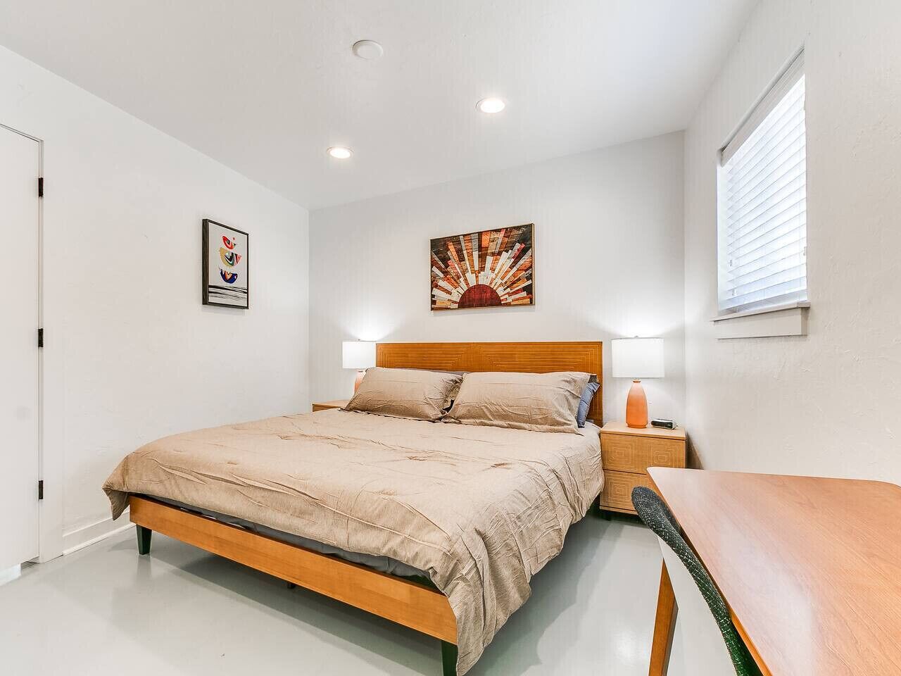 Ein Schlafzimmer mit Bett, Nachttisch, Lampe und einem Kunstwerk an der Wand.
