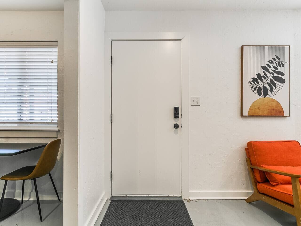 Una habitación con una puerta blanca, un escritorio con una silla y un sillón naranja.