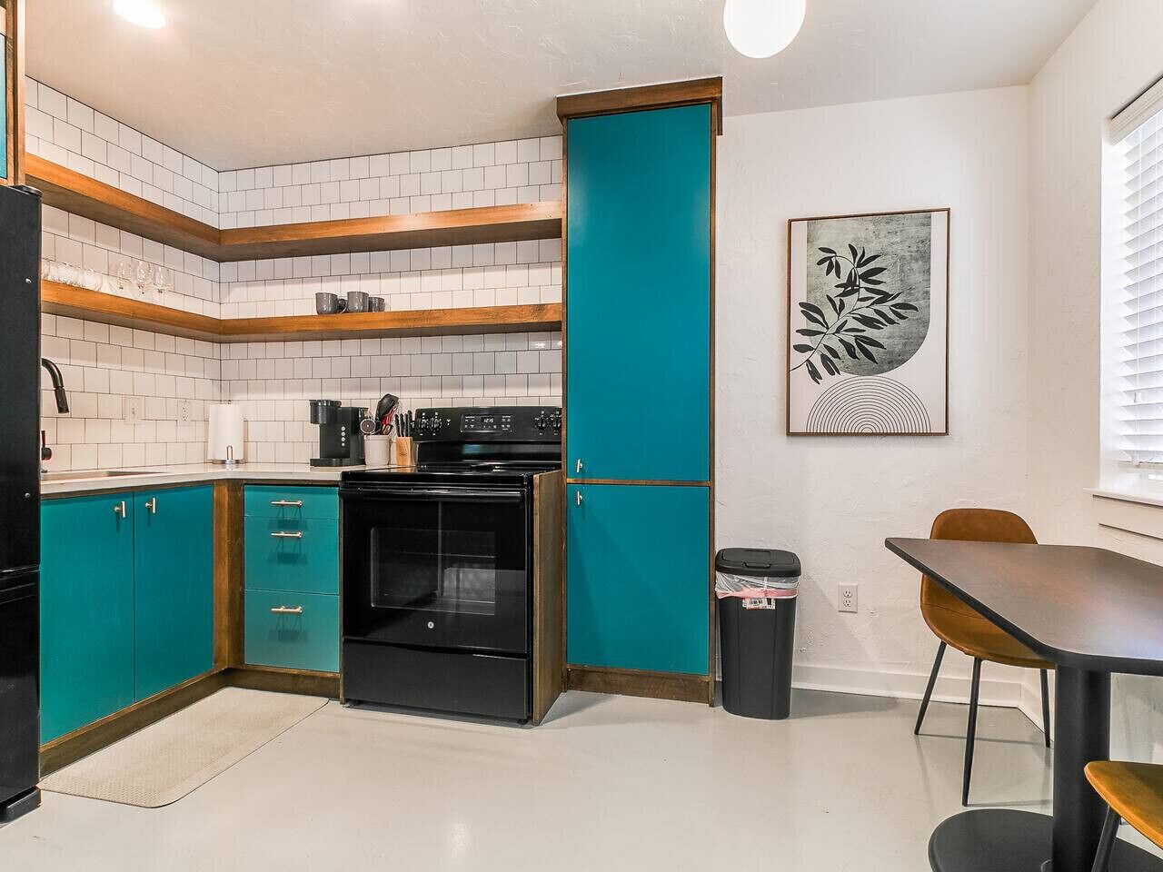 Una cucina con mobili color acquamarina, un piano cottura nero e un'area pranzo con tavolo e sedie.