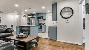 A modern living room with a leather sofa, a wooden coffee table, and a kitchen area with blue cabinets and stainless steel appliances. - Beautiful 2-Bedroom Near Wheeler (Oklahoma City)