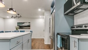 A modern kitchen with a central island, stainless steel appliances, and a view into the dining area. - Beautiful 2-Bedroom Near Wheeler (Oklahoma City)